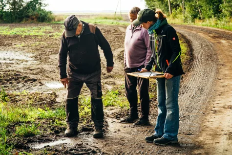 Vermessungsingenieurin von GOLNIK & PARTNER bespricht mit zwei Landwirten einen Plan am Feldrand