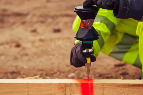 Absteckung eines Punktes mit Prisma und rotem Laserpunkt auf einem Holzbrett des Schnurgerüsts