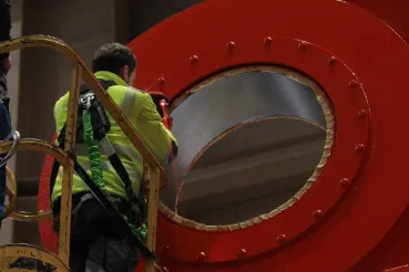 Employee on a lifting platform measuring the flange of a large red component