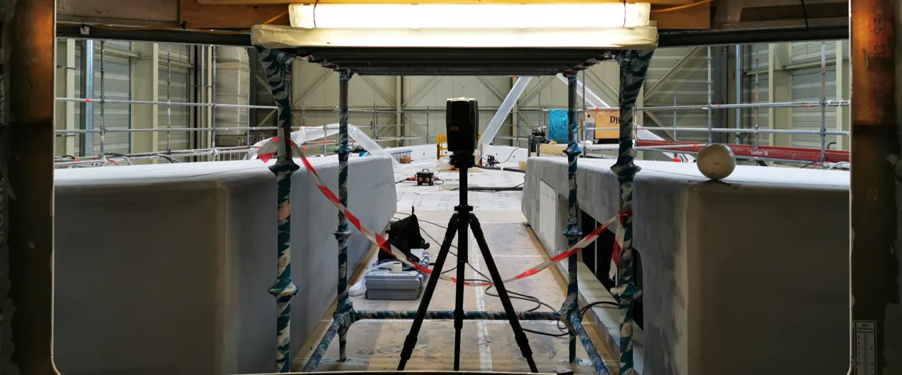 Laser scanner between the superstructures of a yacht under construction, framed by scaffolding