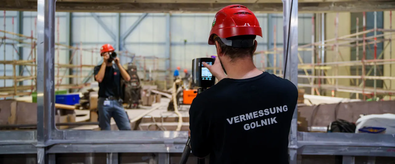 Zwei Mitarbeiter von GOLNIK & PARTNER bei einer 3D-Vermessung mit Laserscanner und Kamera in einer Werfthalle