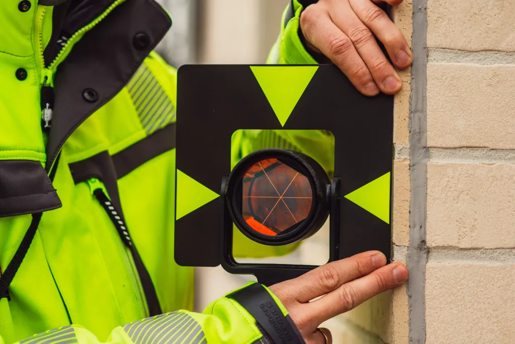 Vermessungsingenieur hält ein Prisma als Messpunkt an eine Hauswand