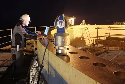 Surveying engineer inspecting a large ring-shaped steel component with a laser tracker