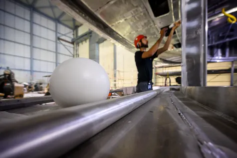 Technician attaching measuring targets to the ceiling of a ship deck, a reference sphere in the foreground